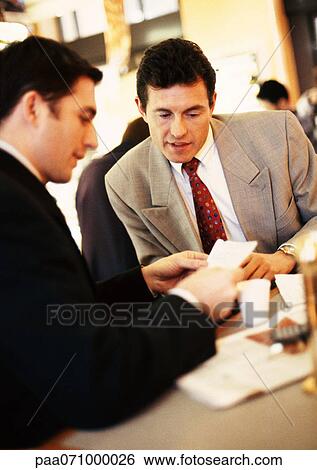 Stock Photograph - Businessmen looking at paper over coffee.. Fotosearch