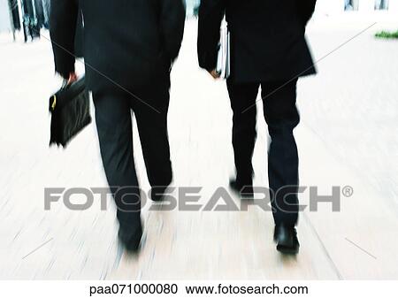 Stock Image - Businessmen walking together, lower section, blurred.. Fotosearch