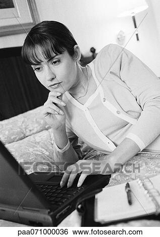 Businesswoman lying on bed, working on laptop computer, b&w. View Large Photo Image Stock Photograph - Businesswoman lying on bed, working on laptop computer, b&w.. Fotosearch