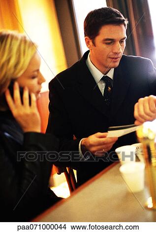 Businesswoman on cell phone next to businessman holding ticket and looking down at watch View Large Photo Image Picture - Businesswoman on cell phone next to businessman holding ticket and looking down at watch. Fotosearch