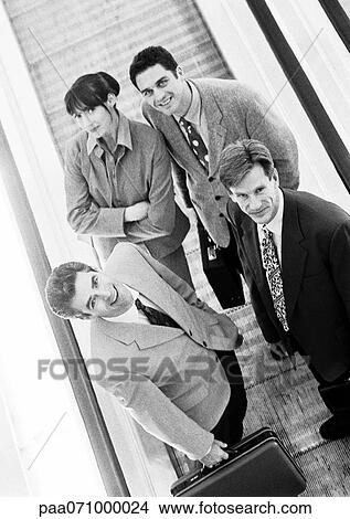 Group of business people on moving walkway looking up at camera, high angle view, b&w. View Large Photo Image Picture - Group of business people on moving walkway looking up at camera, high angle view, b&w.. Fotosearch