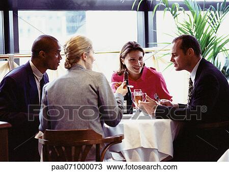 Stock Image - Group of business people sitting at table, eating. Fotosearch