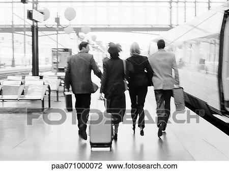 Stock Image - Group of business people walking on train platform, rear view, b&w.. Fotosearch