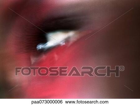 Stock Photograph - Woman's brown eye looking up, red light on face, blurred close up.. Fotosearch