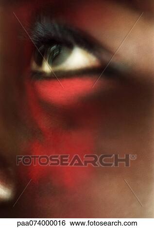 Stock Photograph - Woman's eye looking up with red make-up on face, close-up, blurred. Fotosearch