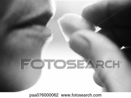 Stock Image - Close up of hand bringing food to woman's mouth, black and white, side view. Fotosearch