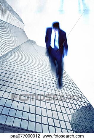 Stock Image - Businessman walking on side of skyscraper, montage. Fotosearch