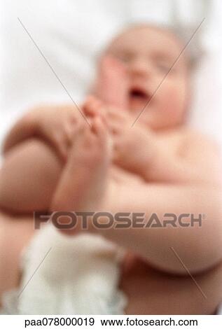 Stock Photo - Baby lying on back, holding feet, blurred. Fotosearch