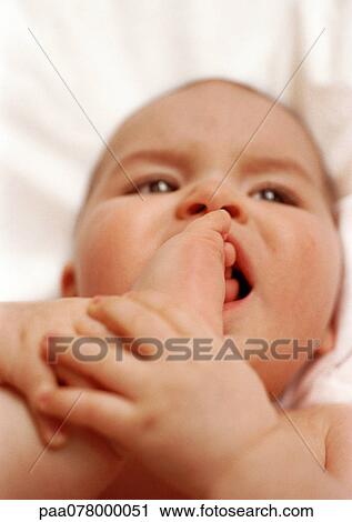 Stock Image - Baby lying on back, putting foot in mouth, close-up.. Fotosearch
