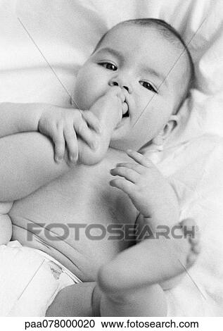 Stock Image - Baby lying on back with foot in mouth, B&W.. Fotosearch
