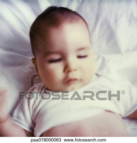 Stock Image - Baby lying on bed, looking down, close-up. Fotosearch