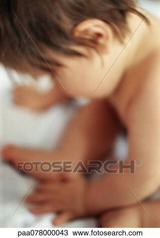 Stock Image - Baby sitting looking down, side view, close-up. Fotosearch