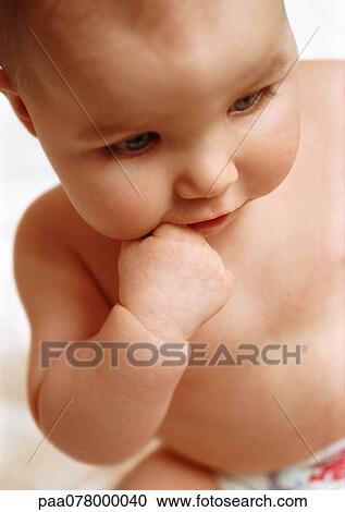 Stock Image - Baby with finger in mouth, looking down, close-up. Fotosearch