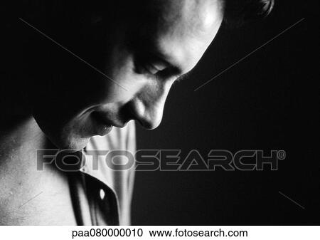 Stock Image - Man looking down, side view, close-up, black and white.. Fotosearch