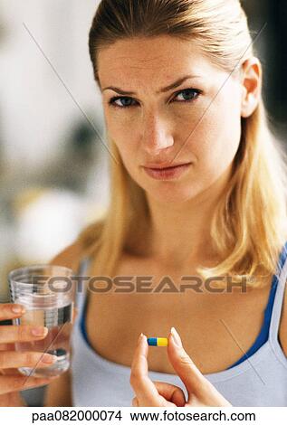 Picture - Woman holding pill and glass, looking at camera.. Fotosearch
