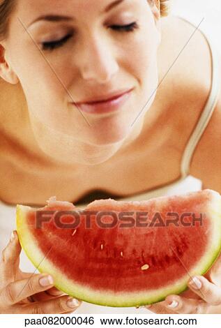 Stock Photograph - Woman holding watermelon slice, eyes closed, high angle view, close-up. Fotosearch