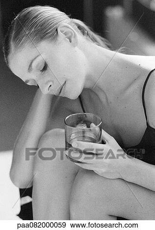 Woman sitting with knees up, holding cup in hand, head tilted down, B&W. View Large Photo Image Stock Photo - Woman sitting with knees up, holding cup in hand, head tilted down, B&W.. Fotosearch