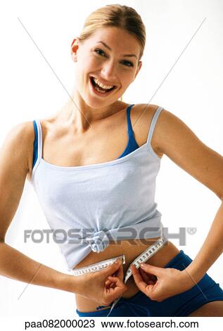 Stock Image - Woman smiling, measuring waist with measuring tape.. Fotosearch