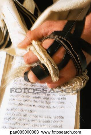 Stock Image - Close up of Jewish man's hand, wearing Tefillin, with Torah. Fotosearch