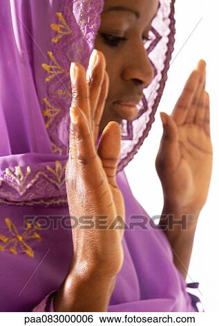 Stock Photograph - Muslim woman wearing veil holding hands up in prayer, close-up. Fotosearch