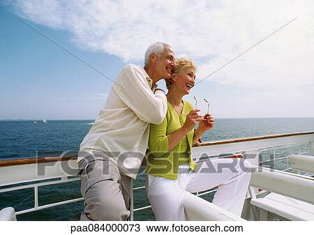 Stock Image - Mature couple leaning against railing, smiling.. Fotosearch