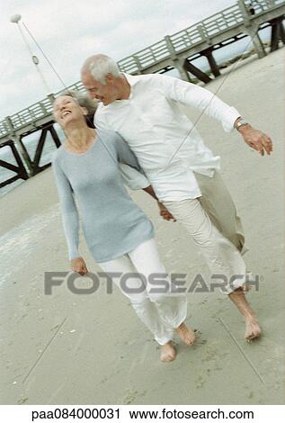 Mature couple walking barefoot and holding hands on the beach View Large Photo Image Stock Image - Mature couple walking barefoot and holding hands on the beach. Fotosearch