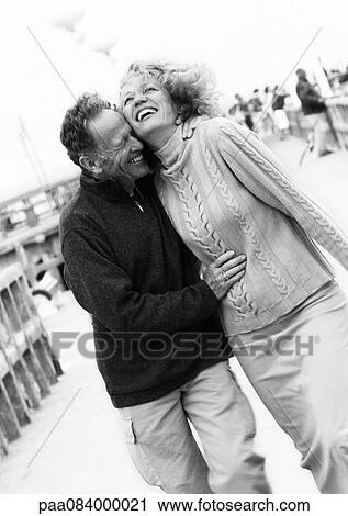 Stock Image - Mature couple walking down boardwalk, laughing, B&W.. Fotosearch