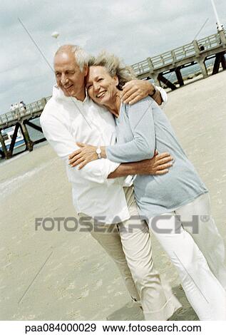 Stock Photo - Mature couple walking with arms around each other on the beach. Fotosearch