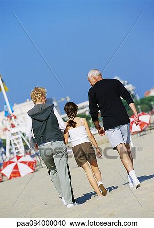 Stock Image - Mature couple walking with girl on the beach, rear view, full length. Fotosearch