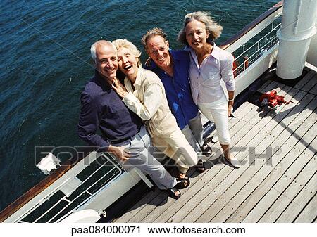 Stock Image - Mature couples standing next to railing of boat, looking at camera, portrait, high angle view. Fotosearch