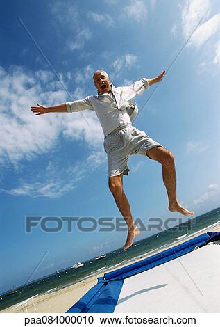 Mature man jumping on trampoline at the beach. View Large Photo Image Stock Image - Mature man jumping on trampoline at the beach.. Fotosearch