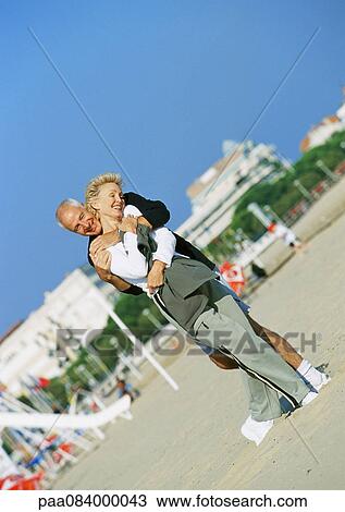 Mature man standing behind mature woman with arms around her on the beach. View Large Photo Image Stock Image - Mature man standing behind mature woman with arms around her on the beach.. Fotosearch