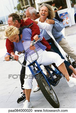 Stock Image - Mature men and women on tandem bike, falling to side, portrait.. Fotosearch