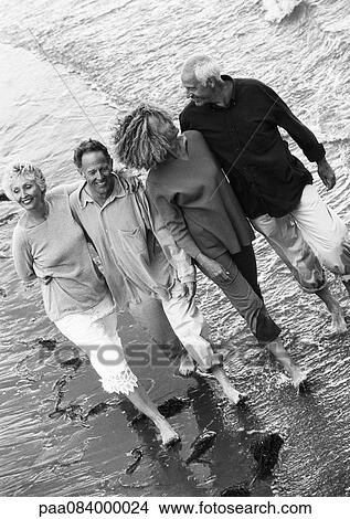 Picture - Two mature couples walking down the beach together, view from above, B&W.. Fotosearch