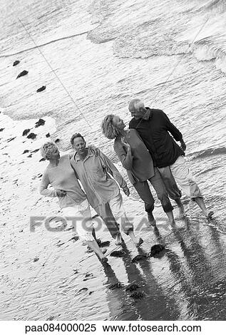 Stock Photography - Two mature couples walking down the beach together, view from above, B&W.. Fotosearch