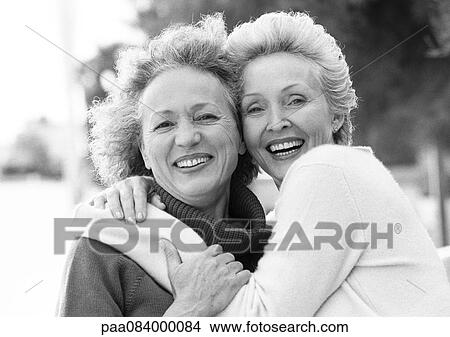 Picture - Two mature women smiling at camera, one with arms around the other's shoulders, portrait, B&W.. Fotosearch