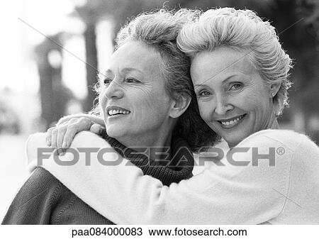 Stock Image - Two mature women smiling, one with arms around the other's shoulders, portrait, B&W.. Fotosearch