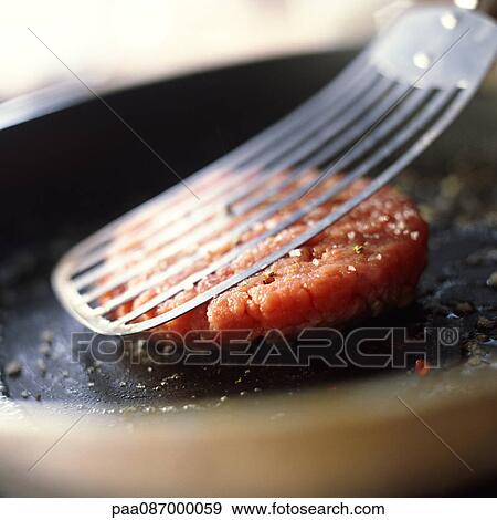 Stock Photo - Close-up of hamburger patty on pan being pressed with spatula. Fotosearch