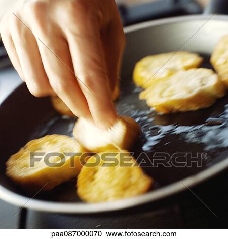 Stock Image - Close-up of hand turning over bread slices in pan, blurry.. Fotosearch
