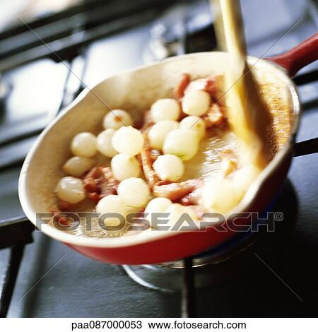 Stock Image - Close-up of onions and bacon being cooked in pan on stove.. Fotosearch