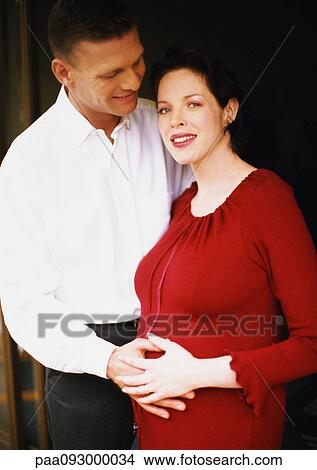 Picture - Man and pregnant woman, both with hands on woman's belly, portrait. Fotosearch