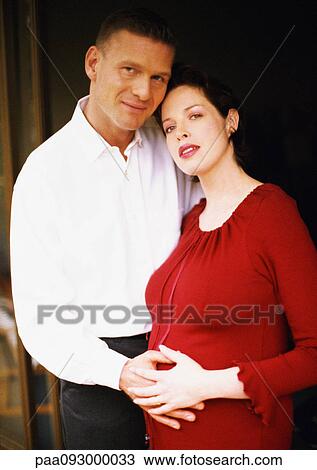 Stock Image - Man and pregnant woman, both with hands on woman's belly, portrait. Fotosearch