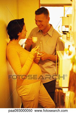 Stock Image - Man and pregnant woman in kitchen, smiling, yellow tone. Fotosearch