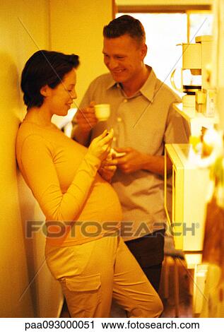 Stock Image - Man and pregnant woman in kitchen, smiling, yellow tone. Fotosearch