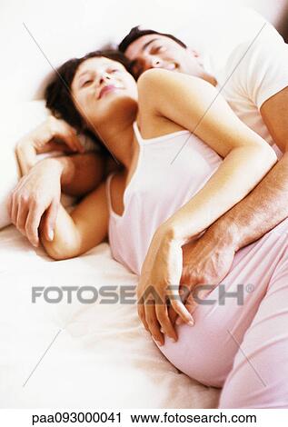 Stock Image - Man embracing pregnant woman in bed. Fotosearch