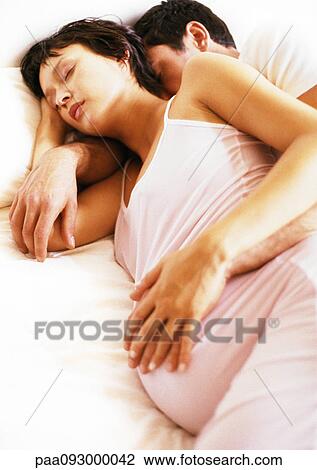 Stock Image - Man embracing pregnant woman in bed. Fotosearch