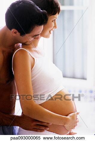 Stock Photography - Man holding pregnant woman's waist and looking over her shoulder, side view. Fotosearch