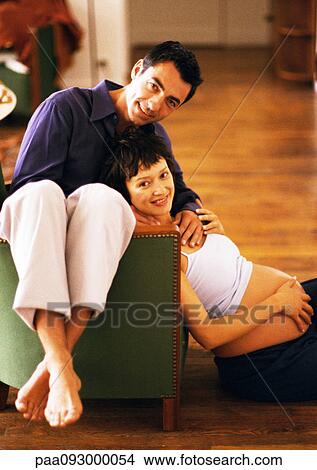 Man sitting backwards on chair and pregnant woman sitting on floor, leaning head on man, portrait View Large Photo Image Picture - Man sitting backwards on chair and pregnant woman sitting on floor, leaning head on man, portrait. Fotosearch