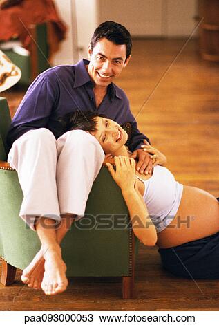 Man sitting backwards on chair and pregnant woman sitting on floor, leaning head on man, portrait View Large Photo Image Stock Image - Man sitting backwards on chair and pregnant woman sitting on floor, leaning head on man, portrait. Fotosearch