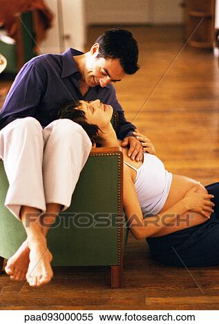Stock Photography - Man sitting backwards on chair and pregnant woman sitting on floor, leaning head on man, portrait. Fotosearch